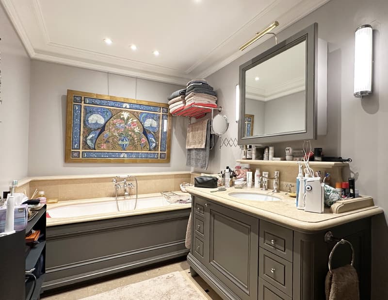 Bathroom with bathtub, sink, large mirror, and cabinet. Framed painting on wall. Towel rack and wall-mounted lights.