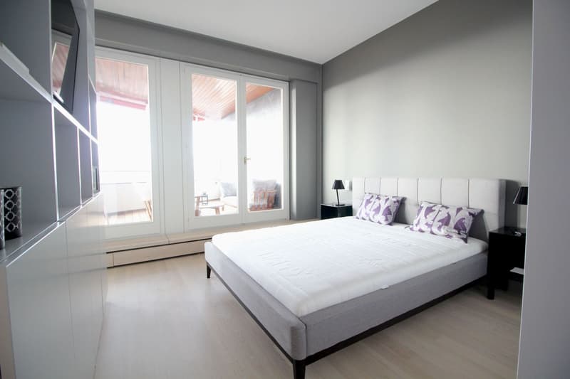 modern bedroom with white walls, wooden floor, large bed, two nightstands, two lamps, large glass doors leading to a balcony