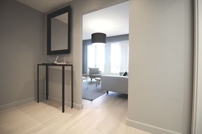 a hall with a table, a mirror and a view to a living room with a sofa and windows