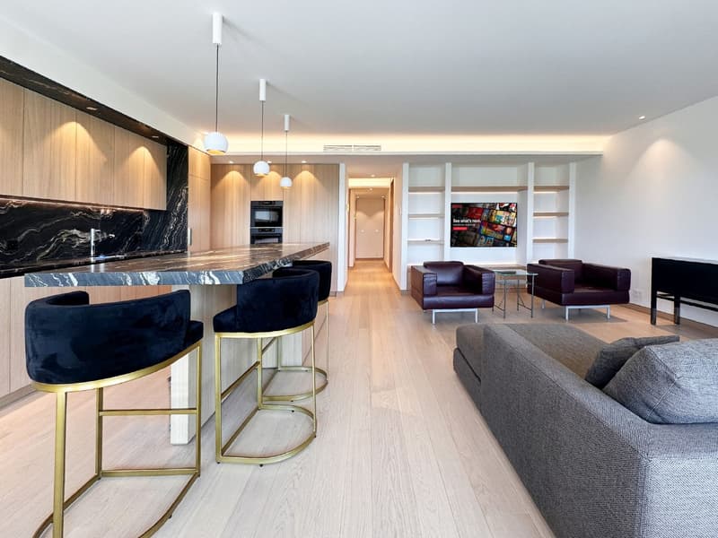 modern kitchen with marble countertop, wooden cabinets, 4 bar stools, living room with couch, 2 armchairs, TV, wooden floor