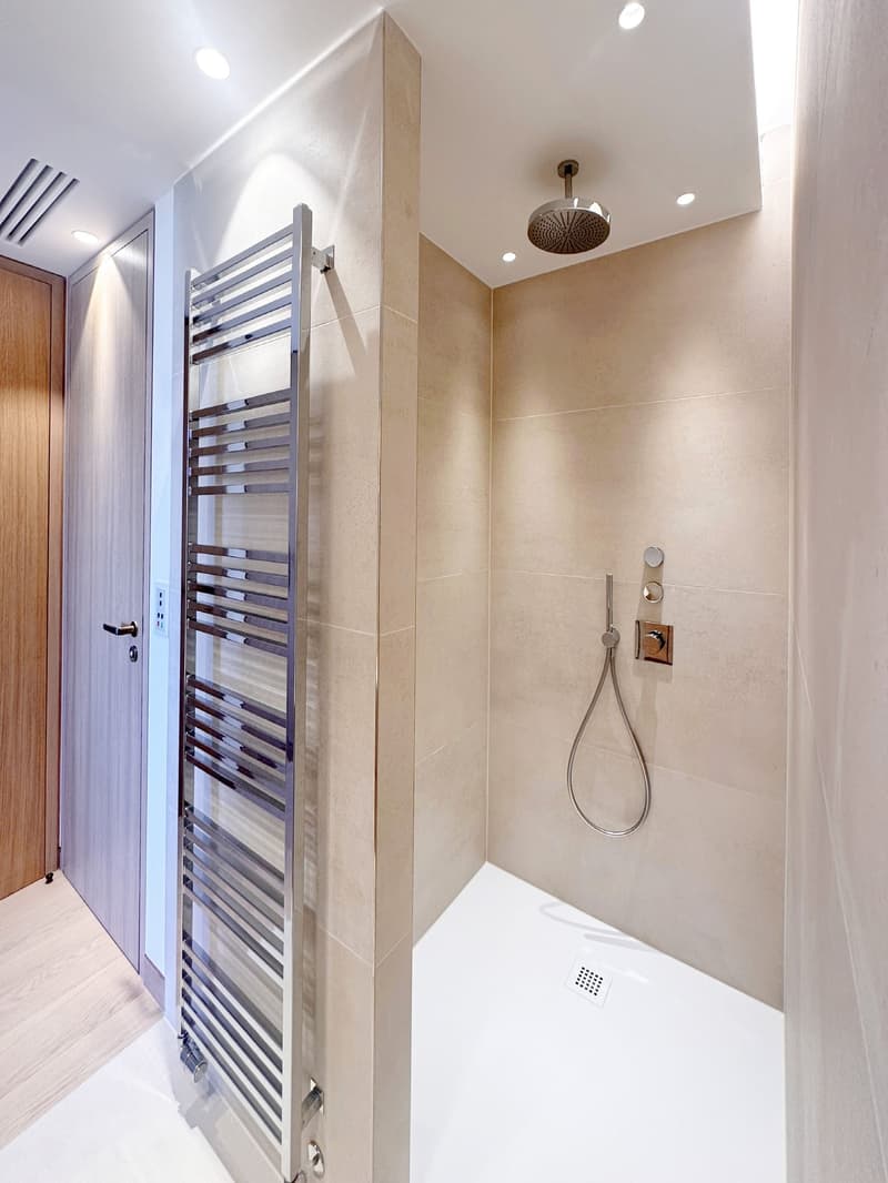 modern shower room with beige tiles, stainless steel shower head, silver towel rack, wooden door
