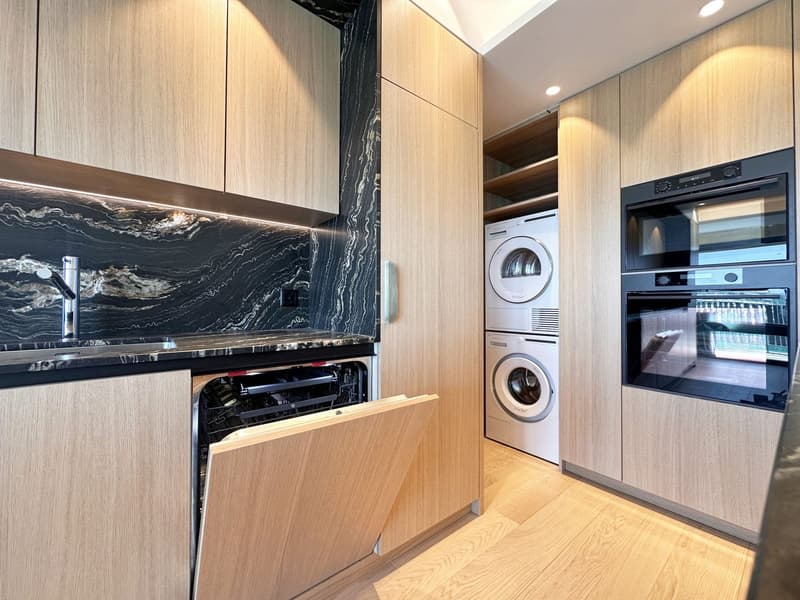 modern kitchen with wooden cabinets, marble countertop, stainless steel sink, dishwasher, washing machine, oven, wooden floor