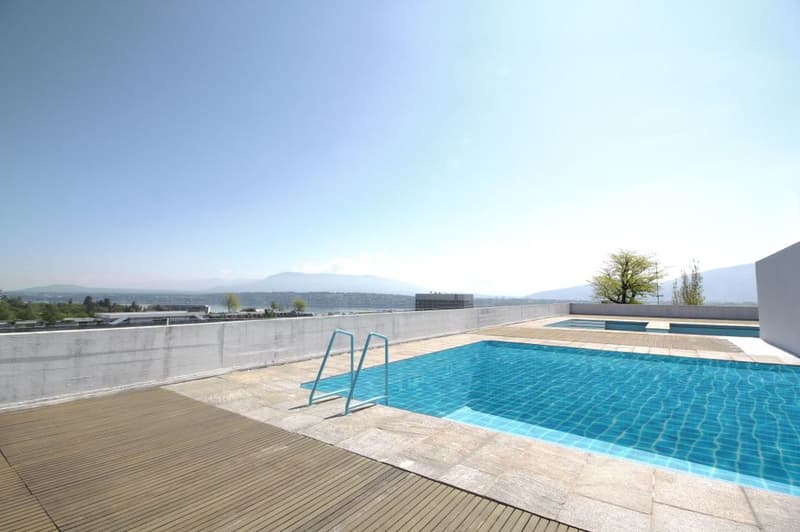 Outdoor swimming pool, wooden deck, concrete wall, clear blue water, handrails, distant view of mountains and water