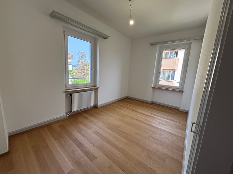 Empty room, wooden floor, two windows, white walls, radiator, wooden trim around the window sill