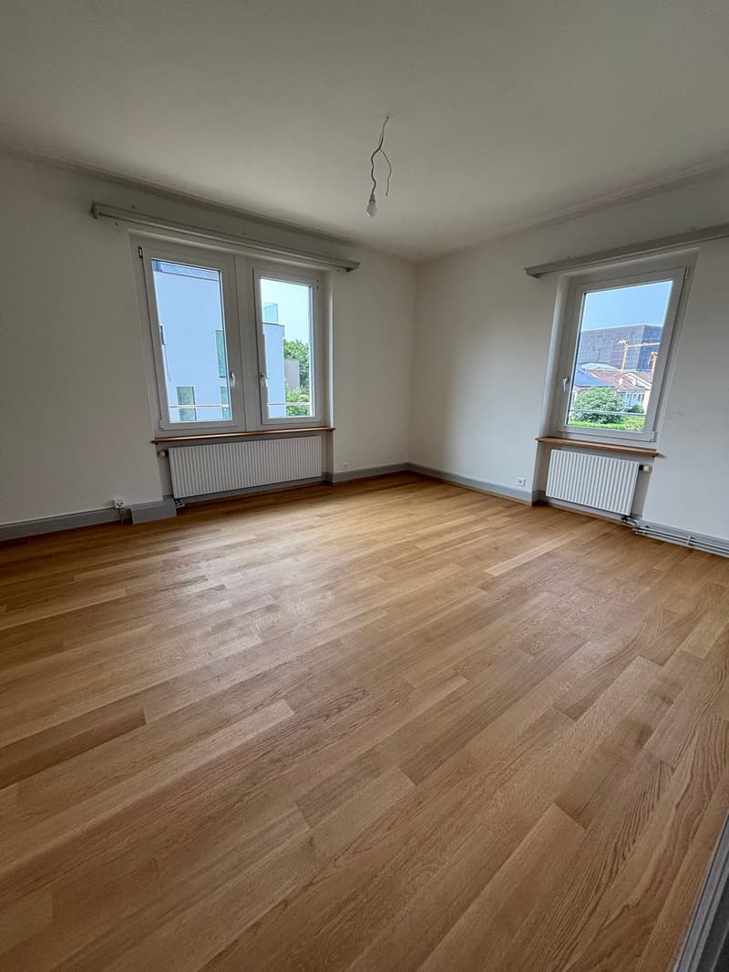empty room, wooden floors, two large windows, radiators beneath the windows