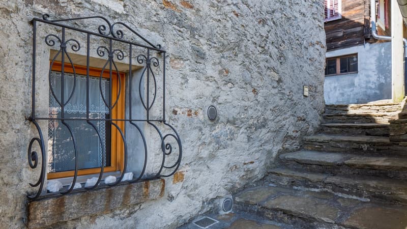 Stone wall, window with black metal grill, stone steps leading up to the entrance