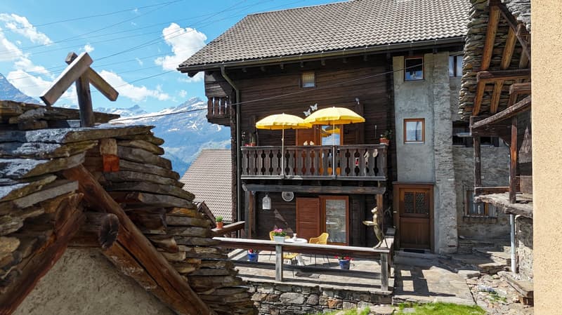 wooden house, stone wall, balcony with yellow umbrellas, table and chairs, mountain view