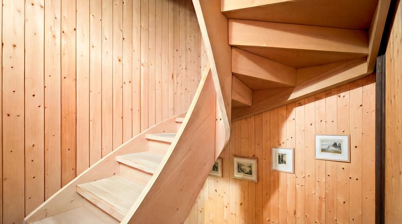 Spiral staircase with wooden steps and wooden walls, and three small framed pictures.