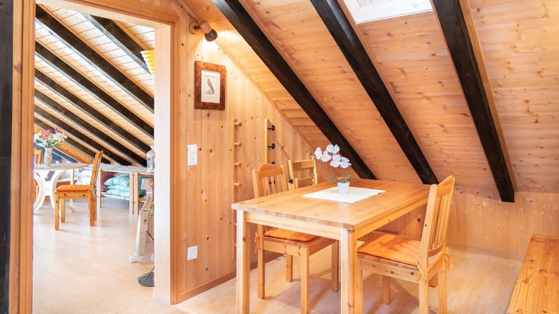 small dining area with wooden desk and 4 chairs, wall with photo, floor with wooden planks