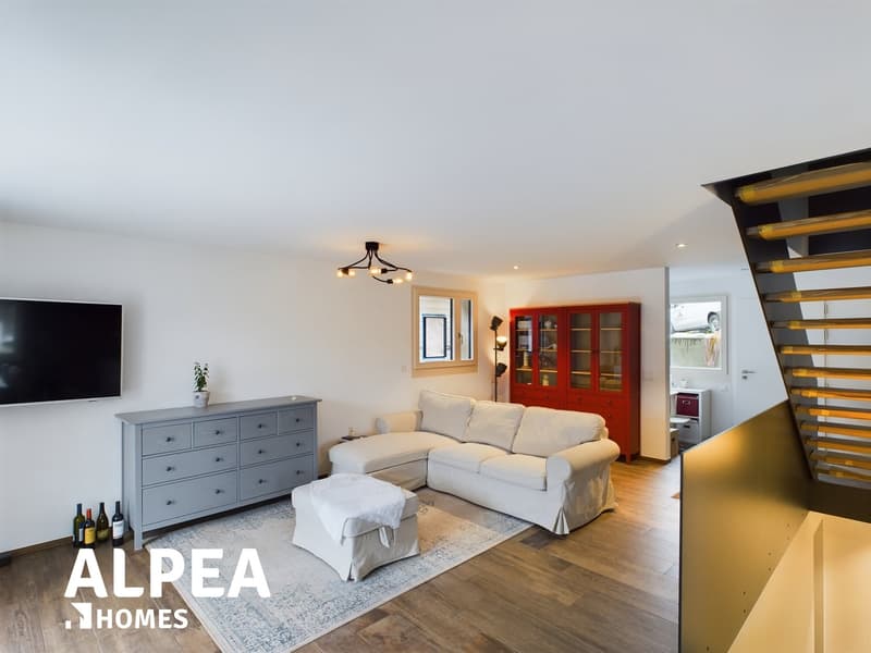 Cozy L-shaped white sofa with covers, grey dresser, floor lamps, carpet, potted plant, TV, wine bottles, chandelier, staircase