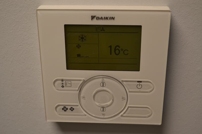 The image shows a Daikin thermostat with a digital display showing the temperature of 16°C. The thermostat has various buttons and controls for adjusting the temperature and settings.