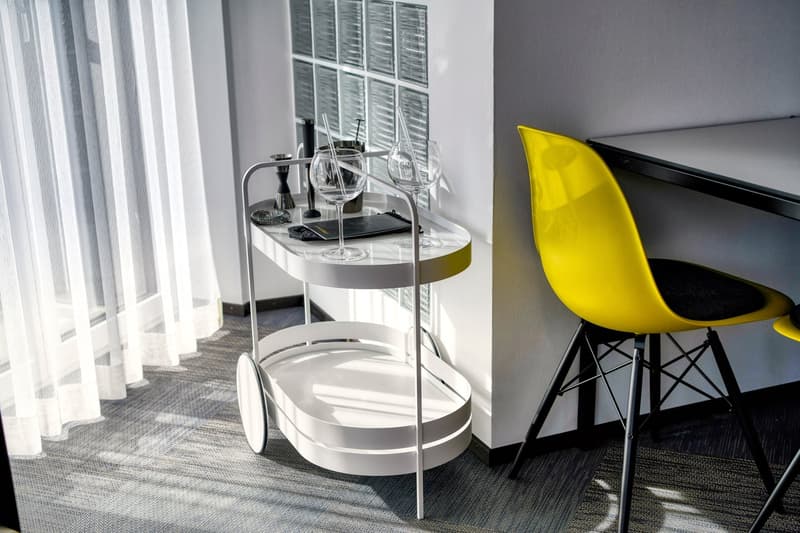White side table with wine glasses, black and yellow chair, curtains, hardwood floor