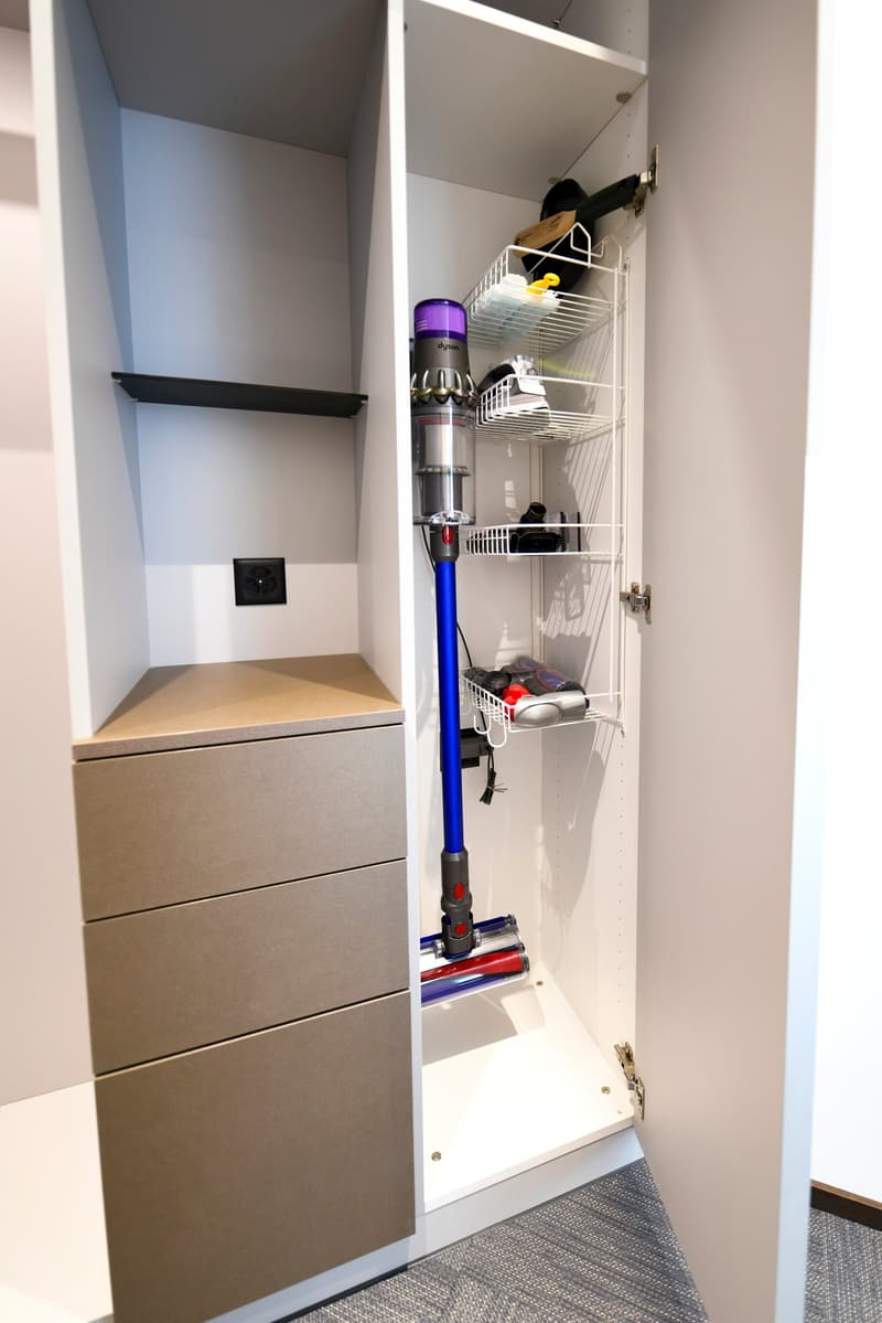 The image shows a utility closet with a vacuum cleaner, storage shelves, and a washing machine or dishwasher visible inside.