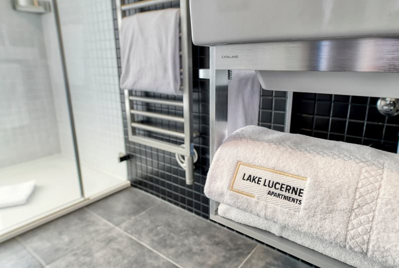 Stainless steel appliances, towels with 'Lake Lucerne Apartments' logo, tiled floor