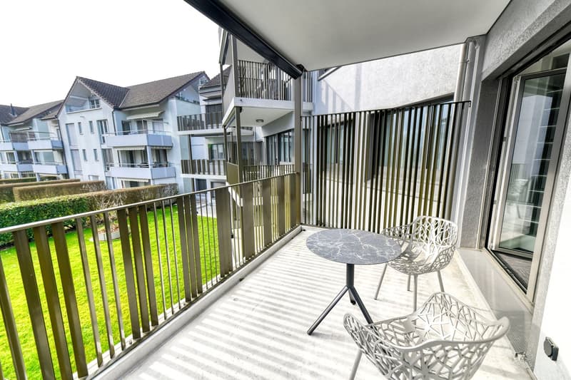 Balcony with a table and chairs, overlooking a grassy area and other apartment buildings