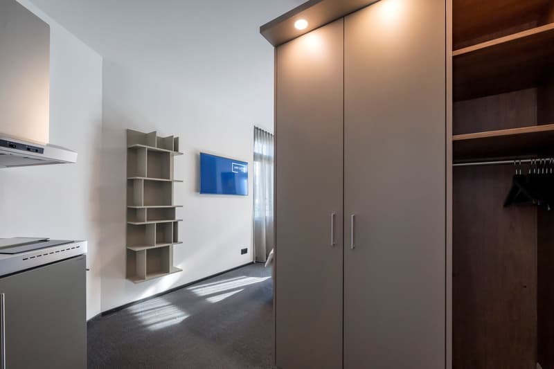 Modern apartment with open floor plan, built-in shelving, large wardrobe closet, and kitchen appliances including a dishwasher