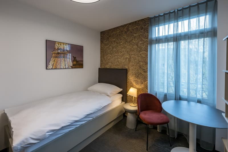 single bed, bedside table, lamp, chair, round table, window with curtains
