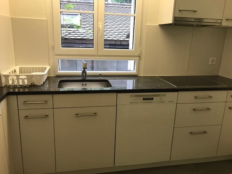 Spacious kitchen with beige cabinets, black granite countertops, a sink, and a dishwasher. There is a window overlooking the exterior of the building.