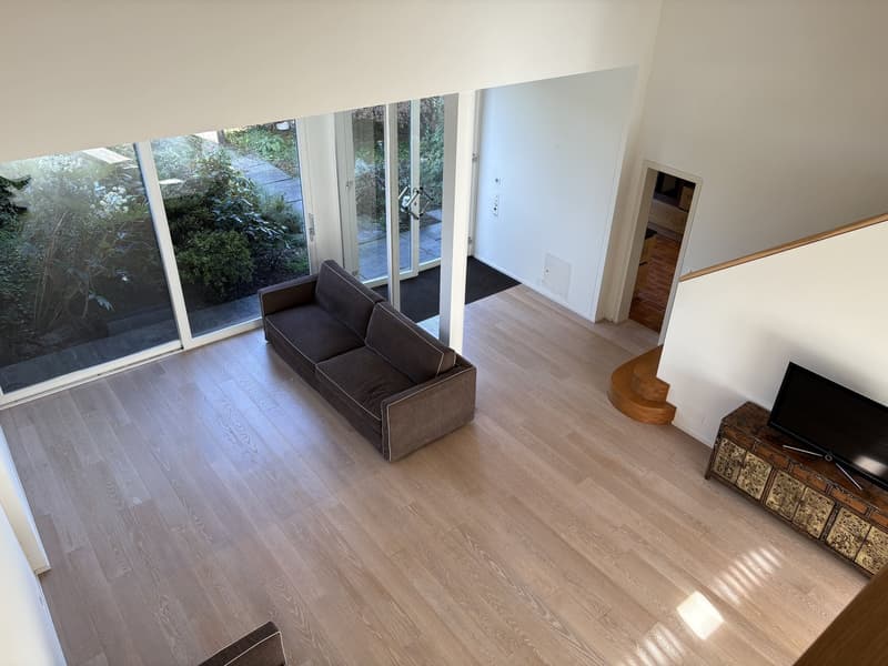 a large couch facing the staircase, wooden floors, glass doors, and a wooden cabinet