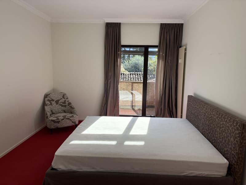 bedroom with bed, red carpet, glass door, white wall, decorative chair
