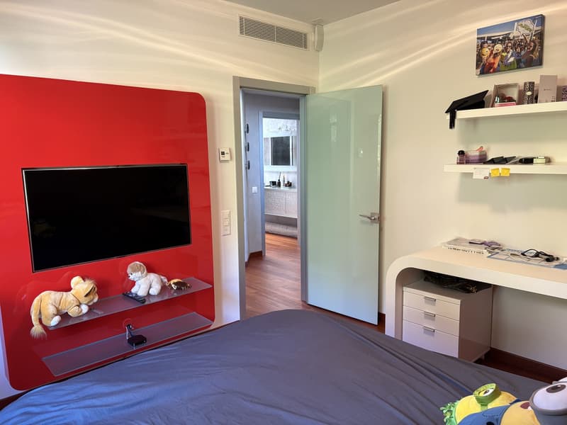 Large bedroom with a bed, desk, shelves, and a mounted television on a red wall.