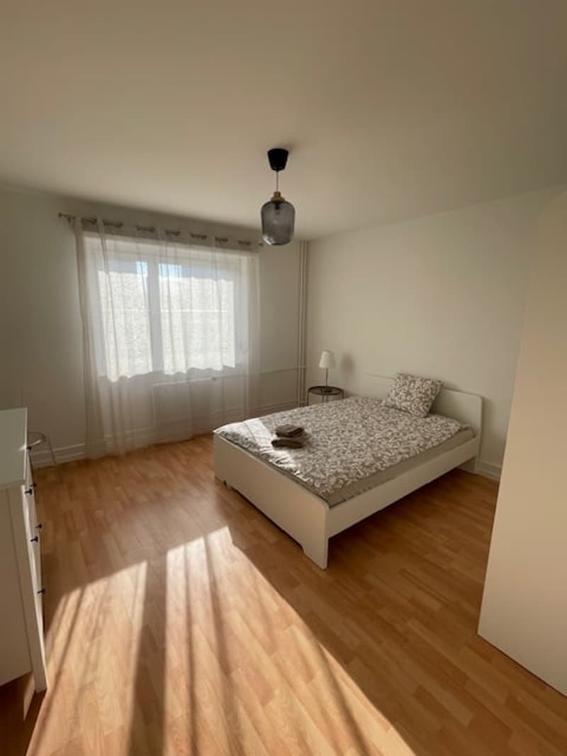 Bedroom with bed, nightstand, lamp, closet, and window with curtains.