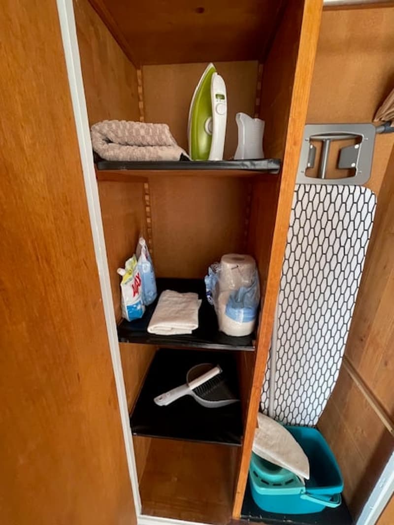 open wardrobe with clothes, cleaning tools, ironing board and iron