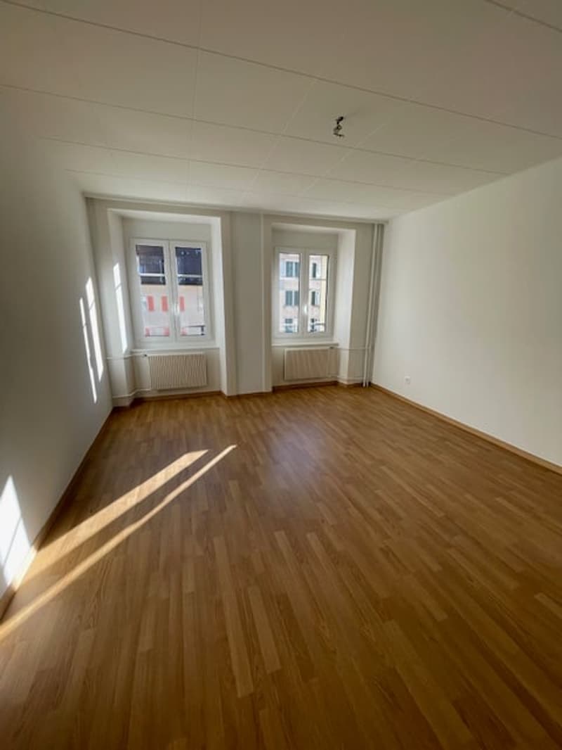 Empty room with wooden floors, white walls, white ceiling, windows, and radiators