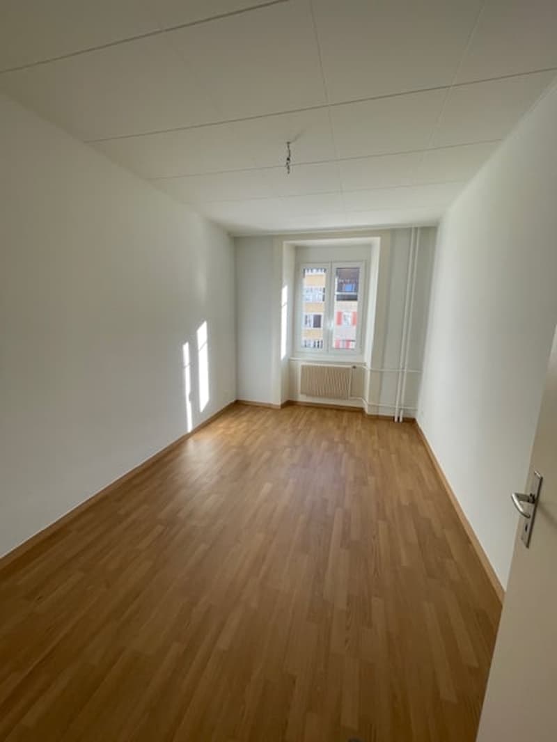 Empty room with white walls, wooden floors, and large window.