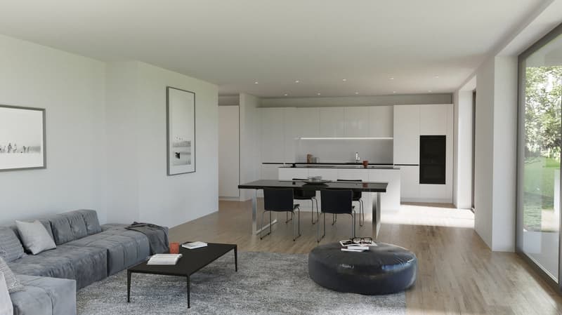 The image shows an open concept living room and kitchen area with a modern, minimalist design. The living room features a large gray sectional sofa, a black coffee table, and a round black leather ottoman. The kitchen has white cabinets, a black counterto