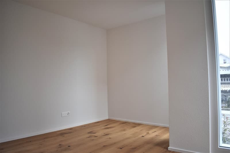 Empty room with white walls, wooden floor, window with outdoor view