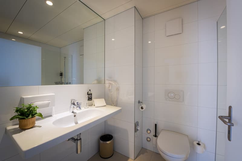 Modern bathroom with white tiles, large vanity sink, shower stall, and toilet