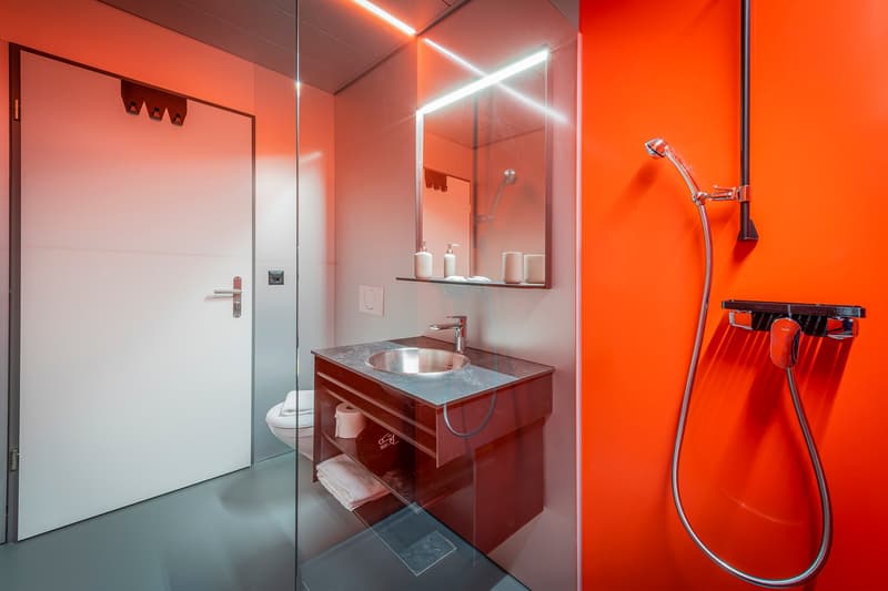 Modern bathroom with red and white color scheme, vanity with sink, mirror, shower with glass enclosure, and towel hooks on the wall