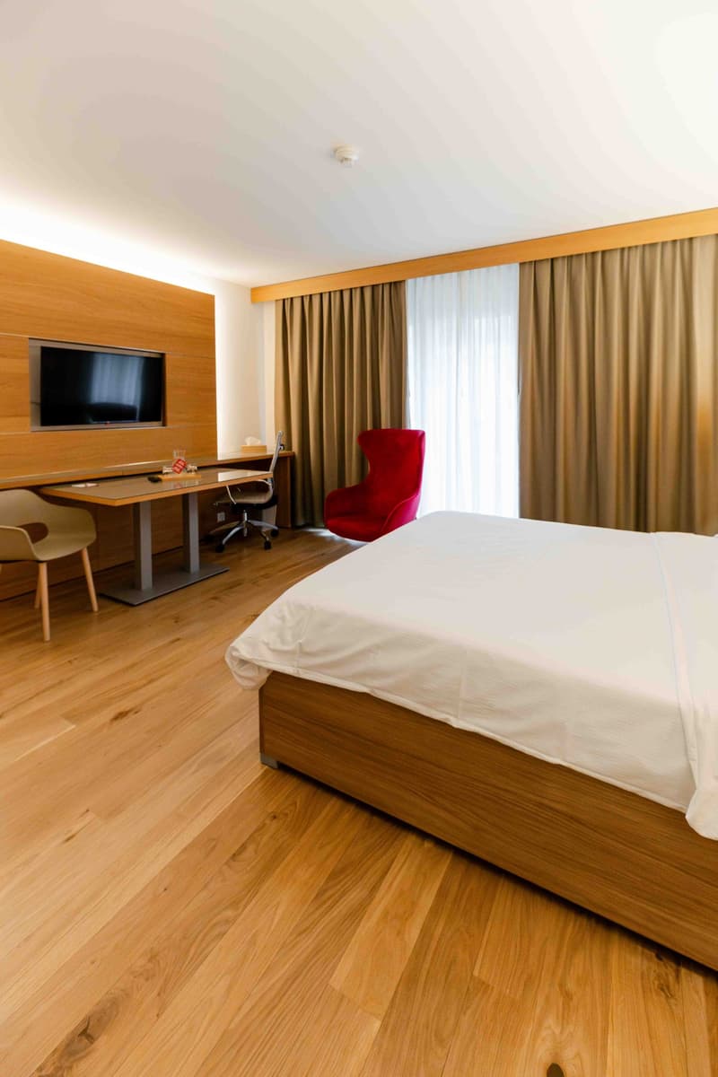 modern bedroom with wooden floor, large bed, desk, chair, TV, curtains