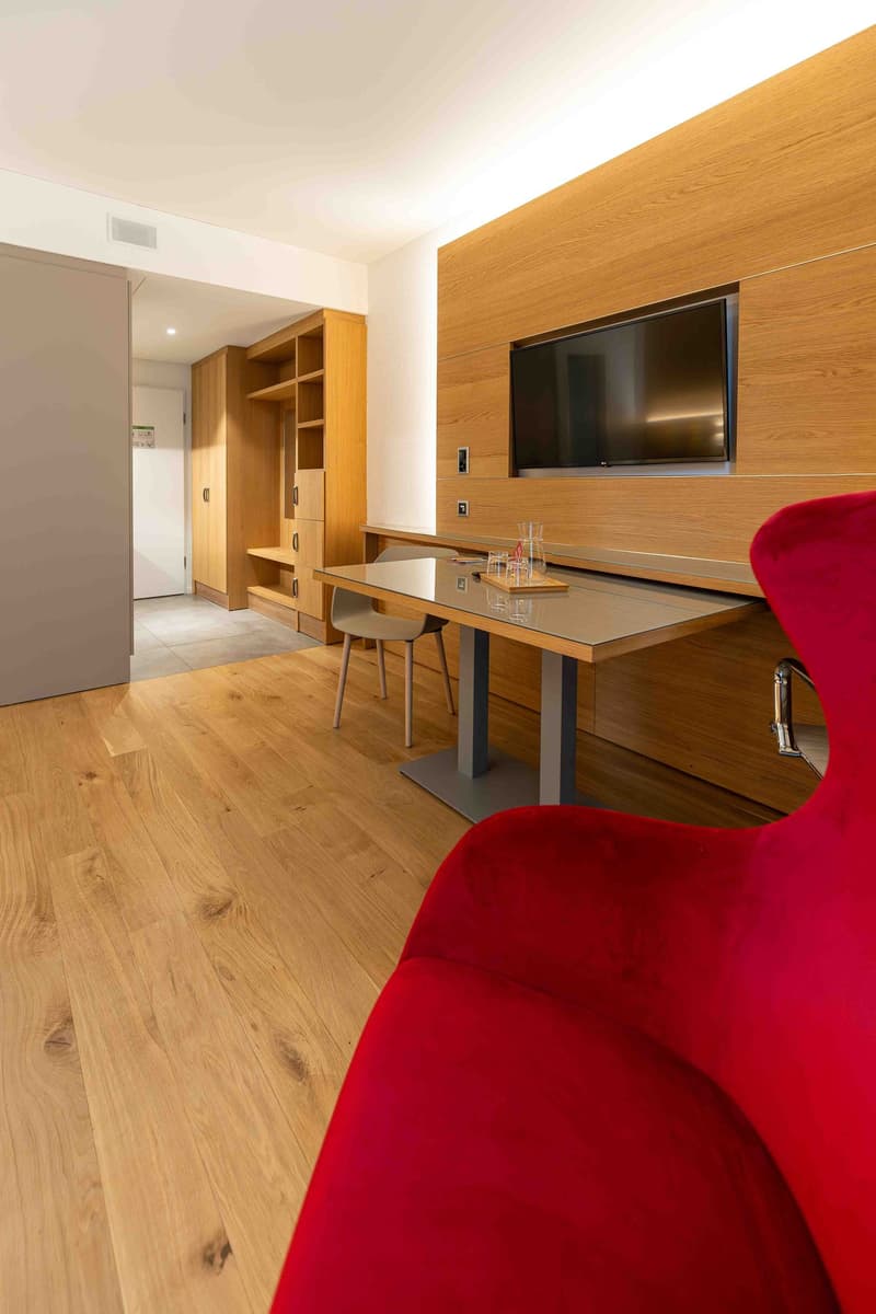 modern room with wooden floor, wooden wall, desk, chair, TV, cabinet, and a door leading to another room