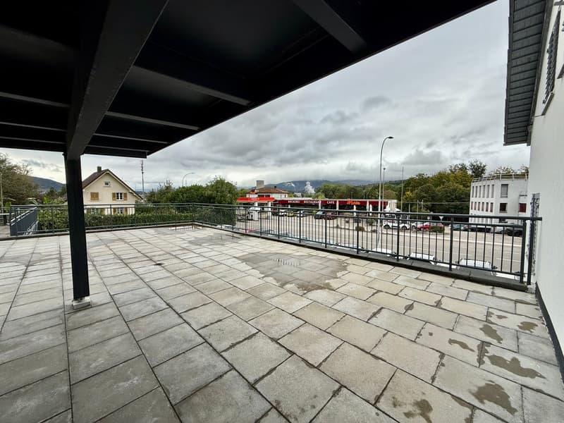 Terrace with a tiled floor and black railings overlooking a road with cars and buildings.