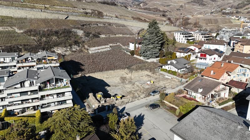 Various residential buildings with terraced design, some undergoing construction, surrounded by hilly vineyards and a construction site.