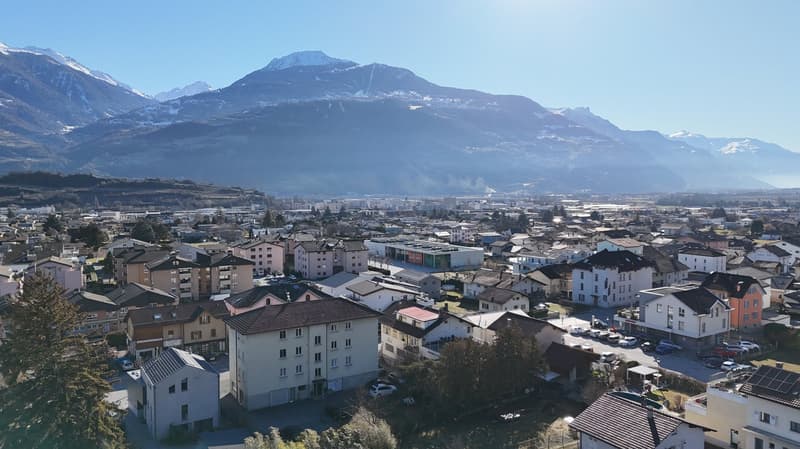Aerial view of a town with many buildings, mountains in the background, and a clear sky.