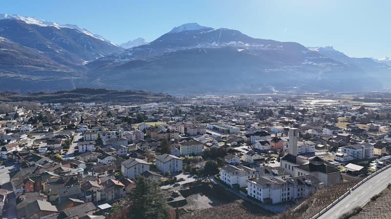 Aerial view of a town with many buildings, surrounded by mountains and trees, with a clear blue sky