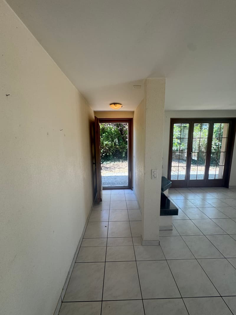 White tiled floor, white walls, single door leading to an entrance with sliding doors, ceiling light, and a small black bench against the wall on the right.