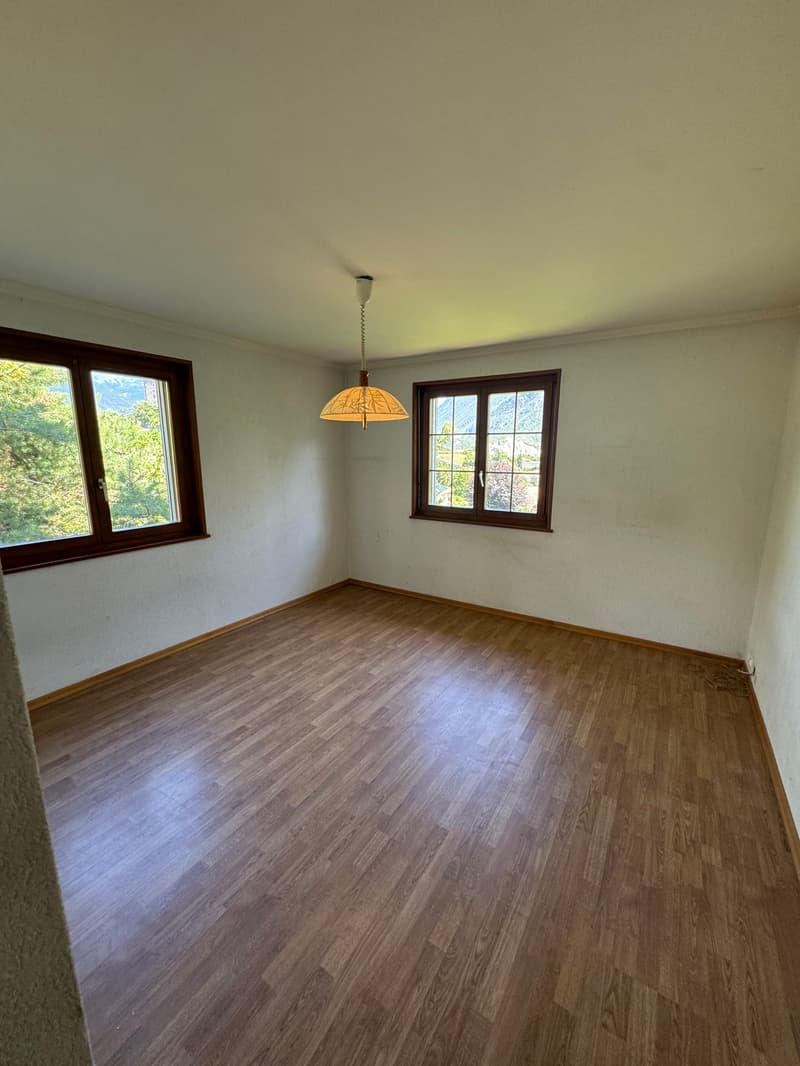 empty room with white walls, wooden floors, two windows, and a chandelier