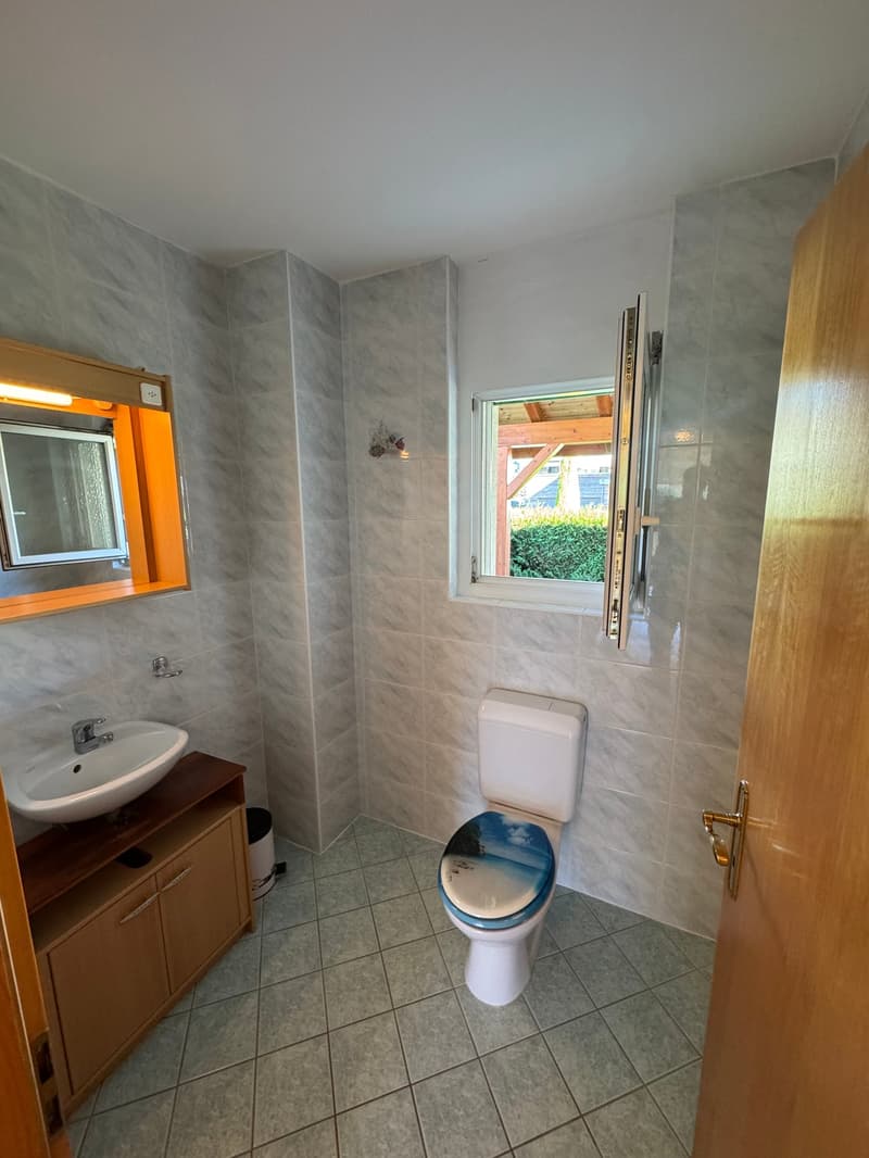 Bathroom with a sink, toilet, mirror, and wooden shelf, tiles, and an open window