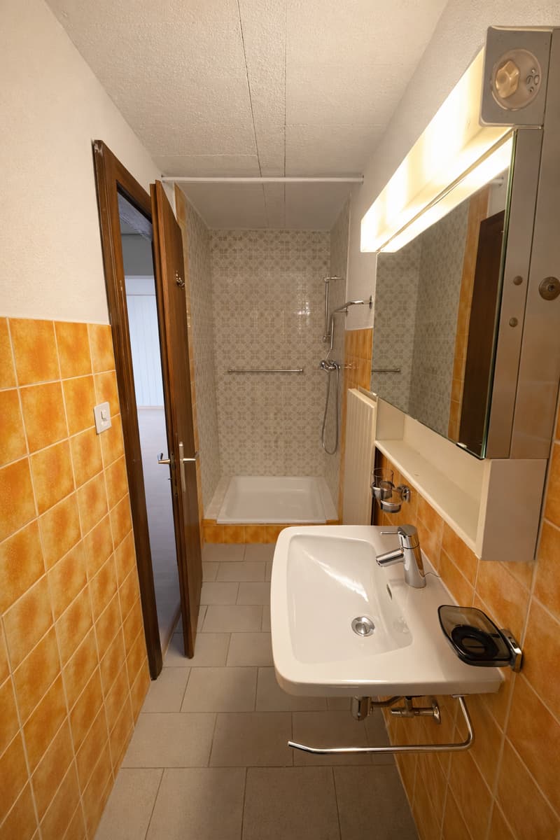 small bathroom with sink, mirror, open shower and yellow tiled walls