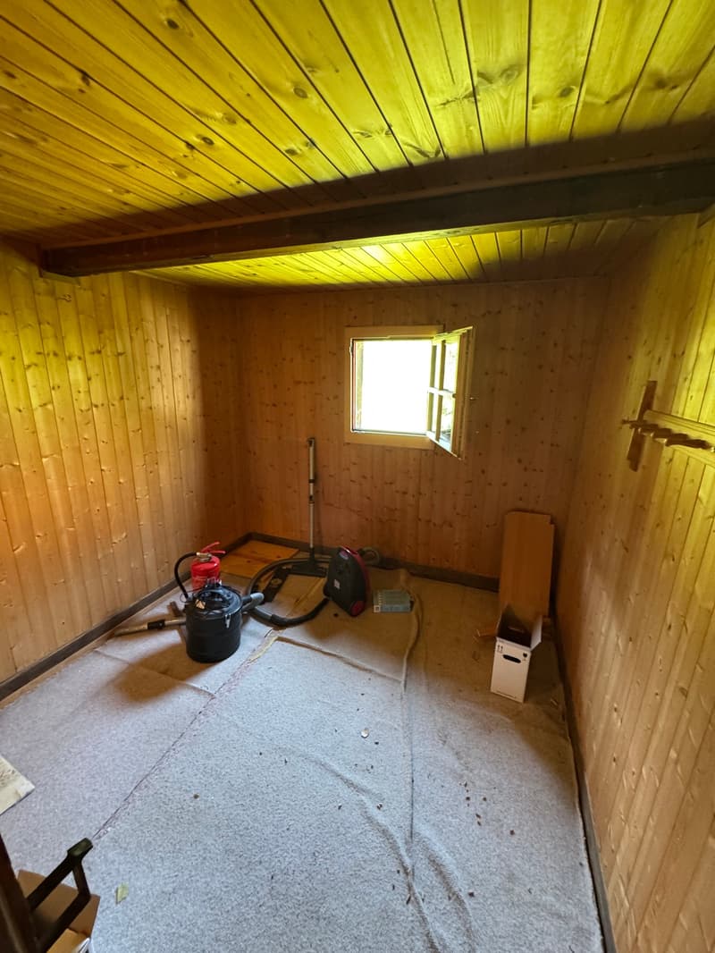 Small wooden room with yellow-tinted walls, a window, and various tools and equipment on the floor.
