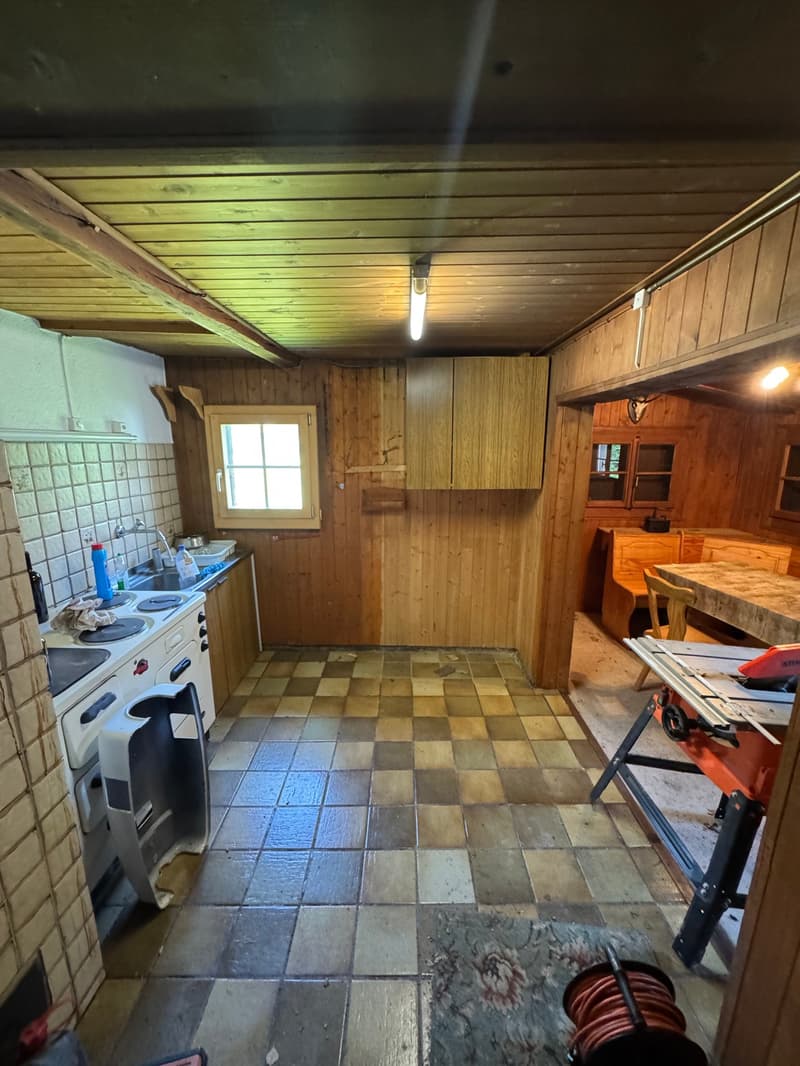 Rustic kitchen with wooden walls and ceiling, tiled floor, stove, and washing machine