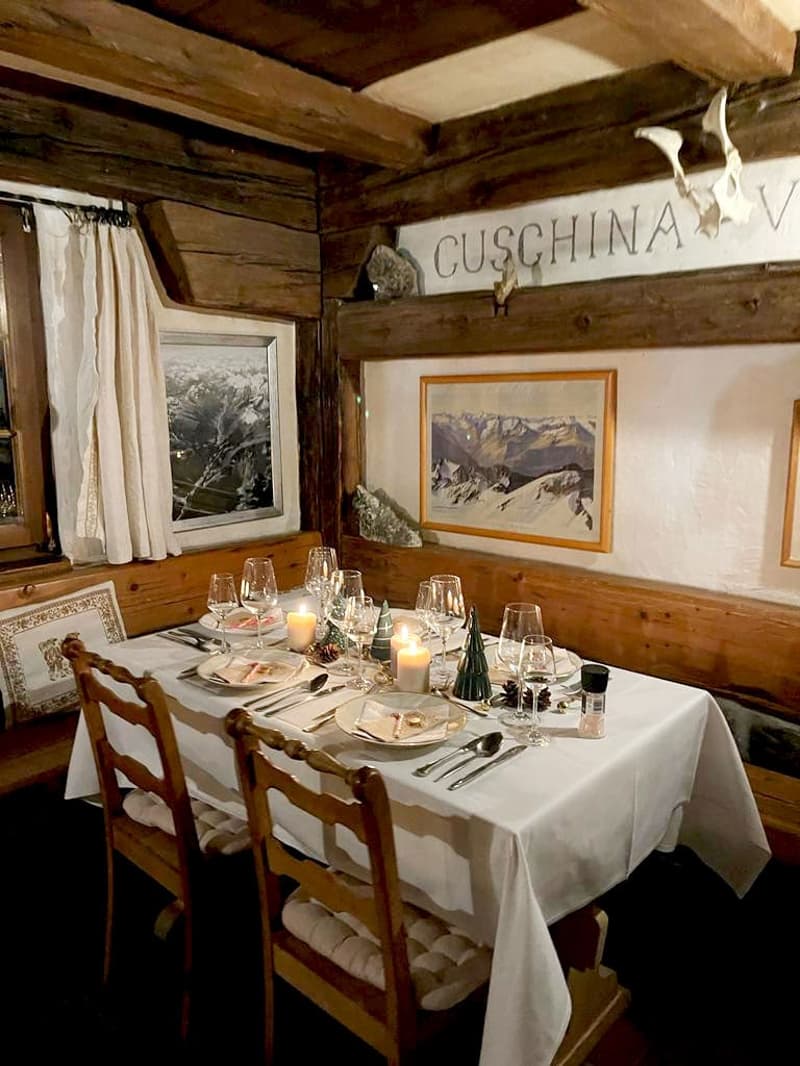 Rustic wooden interior with a dining table set for a meal, framed mountain landscape artwork on the wall, and a sign that says 'Cusching'