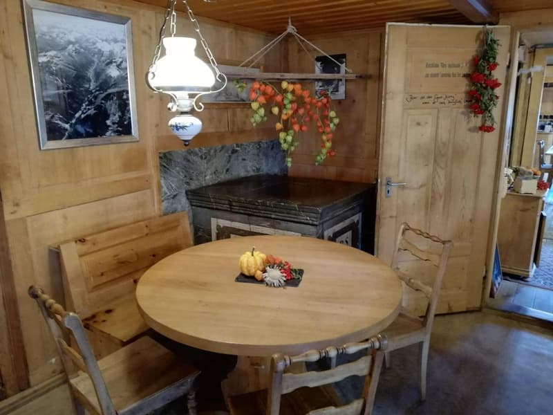 Rustic wooden dining table and chairs, stone fireplace, hanging light fixture, decorative fruit and floral arrangements, wooden walls and ceiling