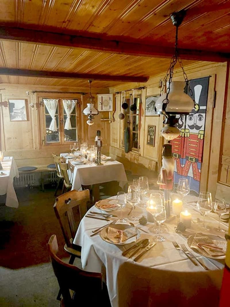 Rustic wooden interior with exposed beams, dining table set with plates and glassware, candles, and a nutcracker figure on display