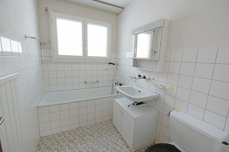 White tiled walls, bathtub, white sink, toilet, white tiled floor, mirror above sink