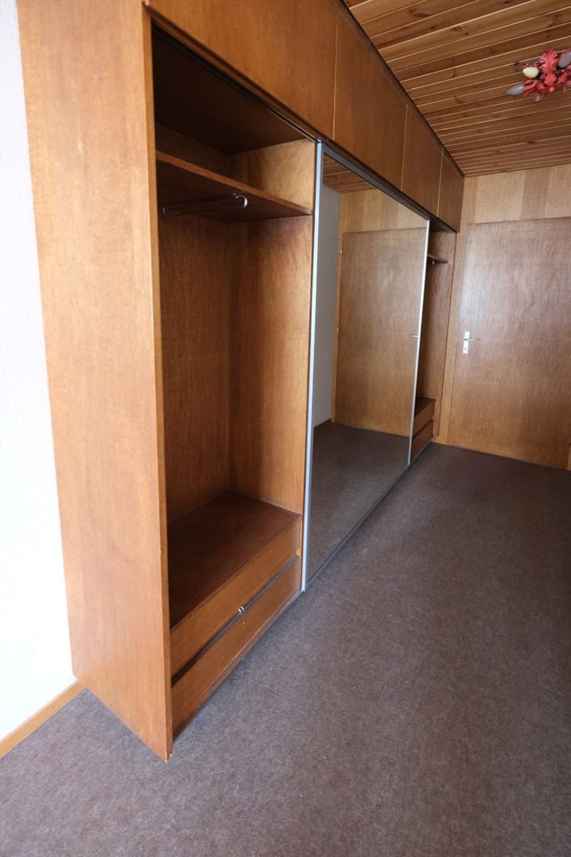 large wooden wardrobe, mirror in wardrobe, hanging rail, wooden floor, brown carpet